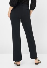 Zwarte, wijde broek met een soepele textuur, voorzien van een rekbare tailleband en twee achterzakken. Gestyled met zwarte strappy sandalen.