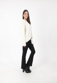 Pull en maille épaisse couleur crème avec des manches larges, associé à un jean noir évasé et des bottines noires à bout pointu. Design simple et épuré.
