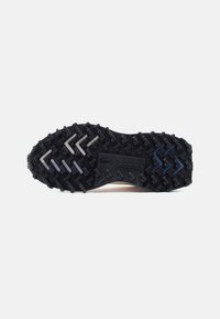 Μαύρη εξωτερική σόλα αθλητικού παπουτσιού με υφασμένα σχέδια, κατασκευασμένη από ανθεκτικό καουτσούκ και με αντιθετικές λευκές και μπλε ζιγκ-ζαγκ λεπτομέρειες.