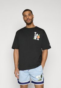 Sort bomulds T-shirt med et grafisk "LA" logo med en orange farve og blade. Designet har en afslappet pasform og korteærmer.