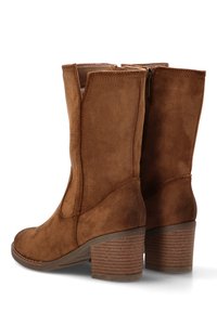 Botas de tobillo de ante marrón con tacón apilado, que presentan paneles laterales y un cierre de cremallera. Las suelas texturizadas ofrecen un agarre adicional.