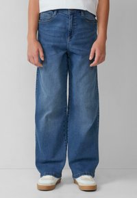 Jeans de pierna ancha en denim azul medio, con una cintura alta, diseño de cinco bolsillos y un ligero desvanecimiento. Combinados con zapatillas blancas.