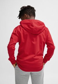 Roter Hoodie aus Baumwollmischung mit langen Ärmeln, einer Kängurutasche und einem lässigen Schnitt, kombiniert mit grauen Jogginghosen.