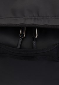 Black backpack with a textured surface. Features two metal clips, adjustable cords, and reinforced stitching along the top edge.