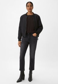 Quilted black bomber jacket with a zip front, black top, dark jeans, and black heeled boots. Smooth texture and fitted design.