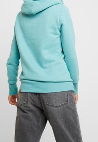 Ljust blå sweatshirt med huva, med ribbade muddar och fåll. Matchad med mörkgrå denimbyxor, som visar fickor och en texturerad yta.