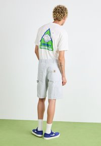 Lichtgrijze cargoshorts met meerdere zakken, gecombineerd met een wit T-shirt met een kleurrijk grafisch ontwerp, en blauwe sneakers.