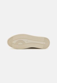Semelle de chaussure en caoutchouc beige avec une surface texturée, dotée de rainures horizontales et de motifs arrondis pour améliorer la traction et la flexibilité.