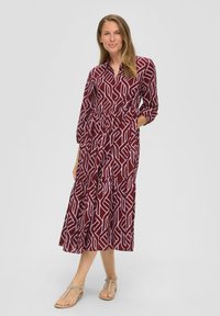 Bordeaux midi-jurk met witte geometrische patronen, knoopsluiting kraag, lange mouwen, elastische taille en gelaagde rok. Draag met lichte sandalen.