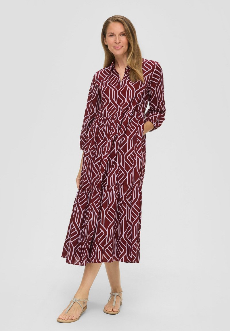 Bordeaux midi-jurk met witte geometrische patronen, knoopsluiting kraag, lange mouwen, elastische taille en gelaagde rok. Draag met lichte sandalen.