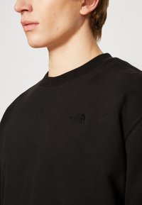 Felpa nera con collo rotondo, polsini a coste e un discreto logo in rilievo sul petto. Realizzata in un tessuto morbido e testurizzato.