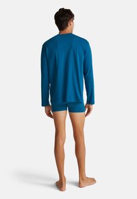 Langsleeve teal shirt en bijpassende shorts, beide in een gladde stof. Het shirt heeft een ronde halslijn en een ontspannen pasvorm.