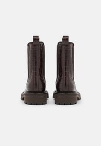 Bottes de cheville en cuir marron avec texture crocodile, dotées de poignées, d'une semelle chunky et d'une plateforme contrastante marron foncé.