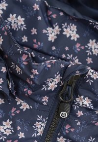 Marineblå stof med blomsterdesign, små rosa og hvide blomster, med en mørk lynlås og teksturerede designdetaljer.