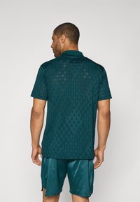 Teal kortærmet polo skjorte med et struktureret diamantmønster, der har en krave-design og en rygventilation. Sammen med matchende shorts.