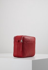 Punainen nahkalaukku, jossa on kaksi vetoketjua, suorakulmainen muoto, sileä pinta ja etutasku. Ominaisuuksiin kuuluu minimalistinen muotoilu ja hienovarainen ompelu.