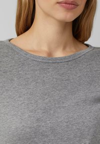 Young woman with long light brown hair wearing a grey crew neck top, visible from lips to upper chest and shoulders.