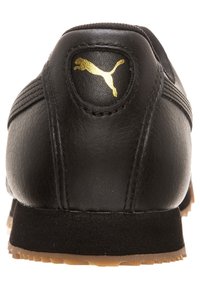 Svart lädersneakerhäl med guld Puma-logotyp, sydda detaljer, svart mellansula och gummirubber yttersula synlig från baksidan.