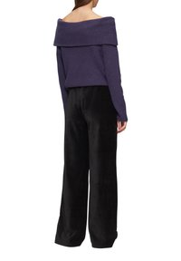 Lila, schulterfreie Strickjacke mit geripptem Kragen, kombiniert mit hoch taillierten, weit geschnittenen schwarzen Samenhosen.