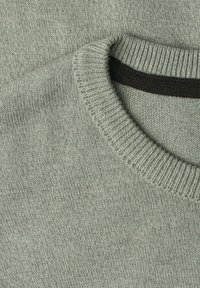 Gros plan sur l'encolure d'un pull tricoté gris clair avec un col côtelé et une étiquette noire rectangulaire à l'intérieur du col arrière.