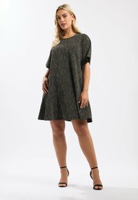 Vihreä lyhythihainen mekko, jossa on hienovarainen kuvio, liehuva hame, pyöreä pääntie ja pehmeä rakenne. Yhdistetty mustiin remmitossuihin.