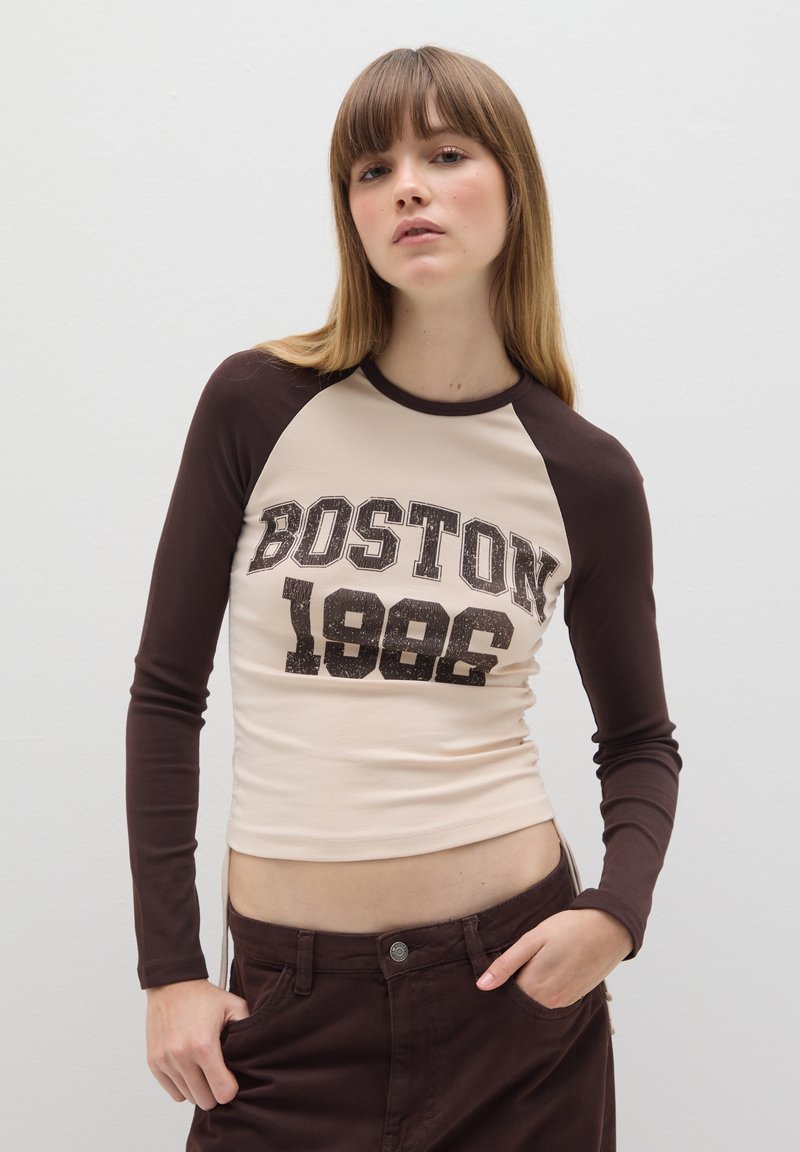 Langärmliges T-Shirt mit beigem Körper und dunkelbraunen Ärmeln, das ein aufgedrucktes "BOSTON 1986"-Grafik im abgenutzten schwarzen Schriftzug zeigt.