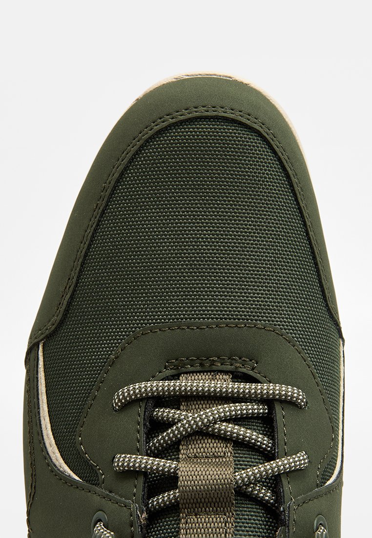 Sneaker verde con un alto in tessuto texturizzato, punta arrotondata e lacci a fantasia. Suola in gomma e accenti chiari lungo i lati.