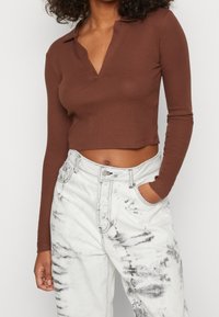 Brązowy prążkowany top z długim rękawem i dekoltem w kształcie V, w połączeniu z białymi dżinsami o wysokim stanie z wzorem tie-dye.