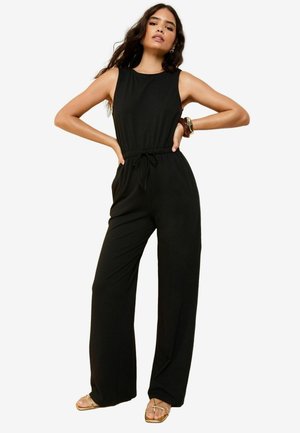 Combinaison sans manches noire à coupe décontractée, avec une taille élastique et des poches latérales. Elle possède une texture lisse et un design à jambe large.
