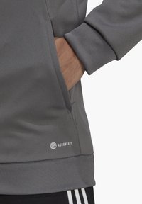 Grauer Fleece-Sweatshirt mit strukturierten Oberflächen, gerippten Bündchen, Vordertasche und einem "AEROREADY"-Logo am unteren Rand.