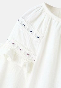 Blusa bianca con delicata ricamatura e dettagli in pizzo sulle maniche, realizzata in tessuto strutturato e con accenti a volant.