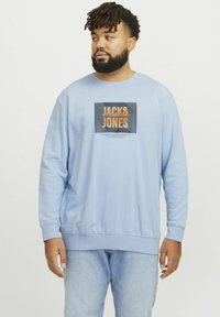 Svetlo modrá mikina vyrobená z bavlnenej zmesi, s grafickým dizajnom na hrudi s nápisom "JACK&JONES" v oranžovej farbe, rebrované manžety a lem, voľný strih.