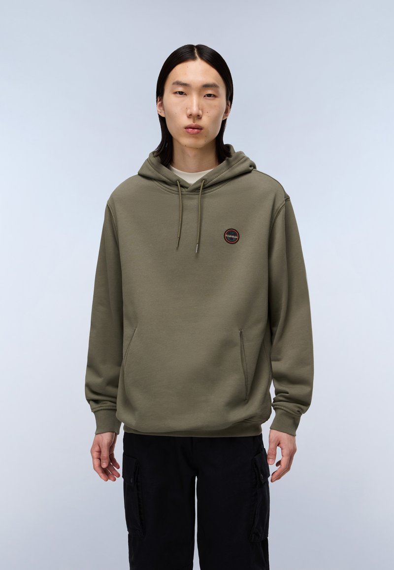 Sudadera verde oliva con un bolsillo frontal, capucha con cordón y un pequeño logotipo circular en el pecho. Textura suave, corte relajado, sin patrones.