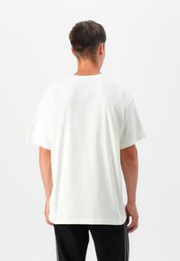 Hvid bomulds T-shirt med korte ærmer og løs pasform, der har en rund halsudskæring og glat tekstur, båret med mørke jeans.