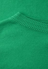 Tissu tricoté vert avec une texture lisse. Présente un col côtelé et un design sans coutures. L'apparence générale est uniforme et vibrante.