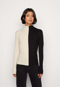 Rebrast pulover s turtleneck ovratnikom v črni in kremni barvi, ki ima obliko v dveh barvah, oprijet kroj, dolge rokave in visok ovratnik.