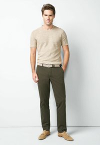 Beige Strick- Kurzarmhemd; oliv gemusterte Hose; hellbraune Loafers mit Quasten; Gürtel mit kariertem Design und Metallschnalle.