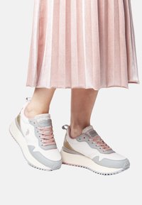 White and light pink sneakers with metallic accents, textured mesh, and a thick sole, paired with a pleated pink skirt.