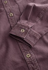 Bomullsskjorta i en mauve nyans, med knäppning fram, spetsig krage och en enda knapp vid manschetten med en texturerad yta.