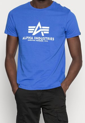 Blaues Baumwoll-T-Shirt mit einem weißen Grafik-Logo, das "ALPHA INDUSTRIES" und Streifen zeigt. Kurze Ärmel, runder Ausschnitt, lässiger Schnitt.