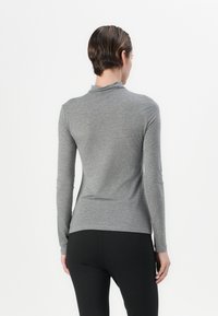 Grå langærmet tætsiddende top med høj hals og glat tekstur. Den har en let indsnøring ved taljen og matches med sorte leggings.