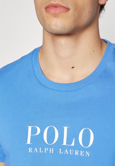 T-shirt de algodão azul com gola redonda, apresentando o texto branco "POLO RALPH LAUREN" impresso na frente, textura suave.