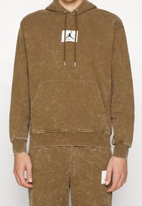 Felpa cappuccio marrone con tasca a marsupio, cuciture a contrasto e un patch con logo sul petto. Realizzata in materiale morbido e strutturato.