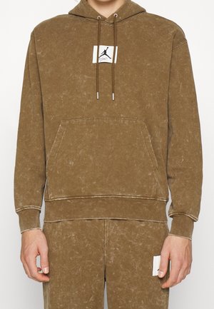Brown pullover hoodie featuring a kangaroo pocket, contrasting stitching, and a logo patch on the chest. Made of soft, textured material.