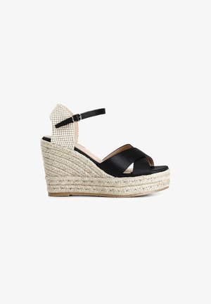 Sandalia con cuña de cuero negro, straps cruzados, suela de estilo espadrille de cuerda y una parte trasera de tela estampada. Detalle de correa ajustable en el tobillo.