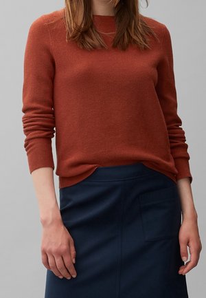 Maglione lavorato a maglia color ruggine con maniche lunghe, scollo rotondo e orlo a costine, abbinato a una gonna blu scuro con tasca laterale.