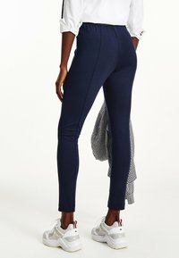 Navy leggings dengan pinggang elastis, potongan ramping, dan aksen jahitan vertikal. Dipadukan dengan sepatu atletik putih dan kain bermotif hitam-putih.