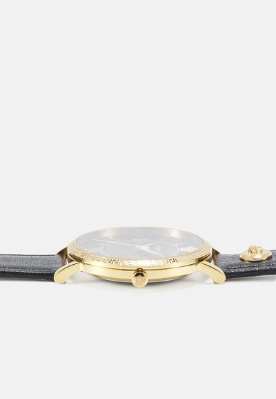 Gold-tone watch with a black leather strap, circular case, textured bezel, and black dial featuring Roman numerals and a crown accent.