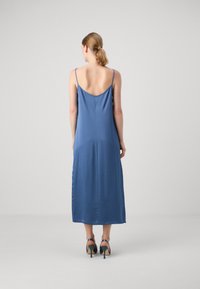 Rochie midi din satin albastru cu bretele subțiri, spate adânc și textură netedă, asortată cu sandale negre cu toc înalt.