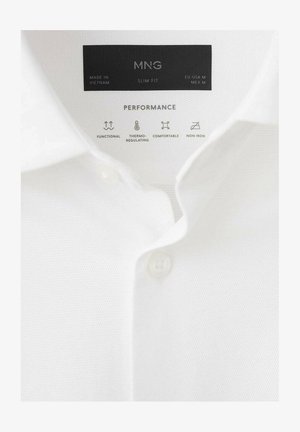 Gulerul cămășii albe cu croială slim, cu etichetă care indică mărimea M, fabricat în Vietnam, și pictograme pentru caracteristici funcționale, termo-reglare, confort și fără nevoie de călcat.